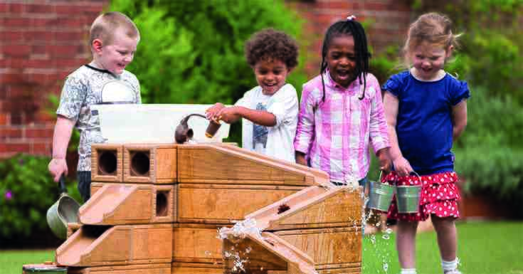Four children playing outdoors with Outlast Ramps, pouring water down the wooden ramps.