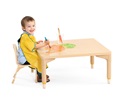 a boy wearing a yellow apron sitting at a table and doing finger painting