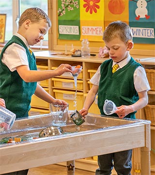Two young boys in green vests playing with water in a sand and water table.