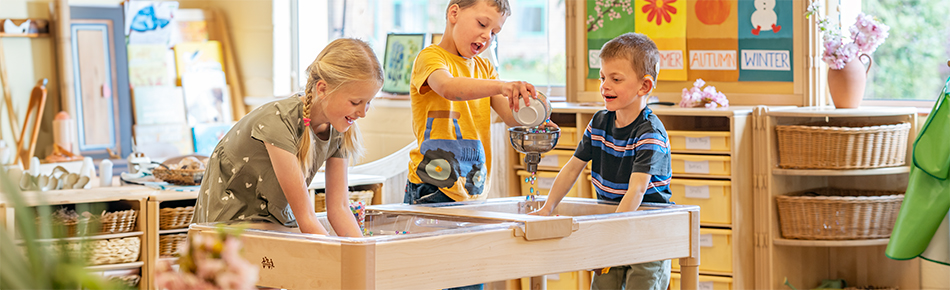 Three children playing with a sand and water table