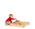 A baby boy in a red shirt scooping wood shaving in the Activity floor tray.