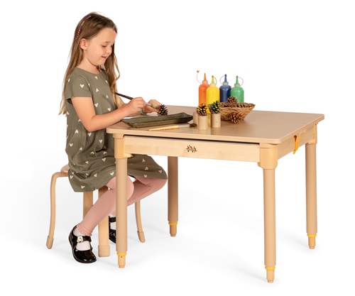 A reception aged girl in a green dress painting pinecones on an Activity tray-table.