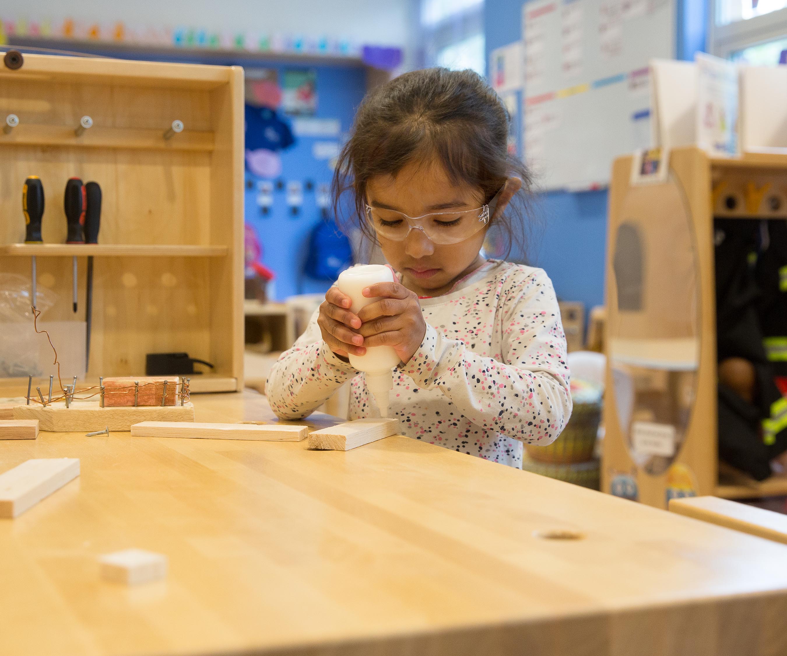 a girl squeezing a glue bottle at a workbench