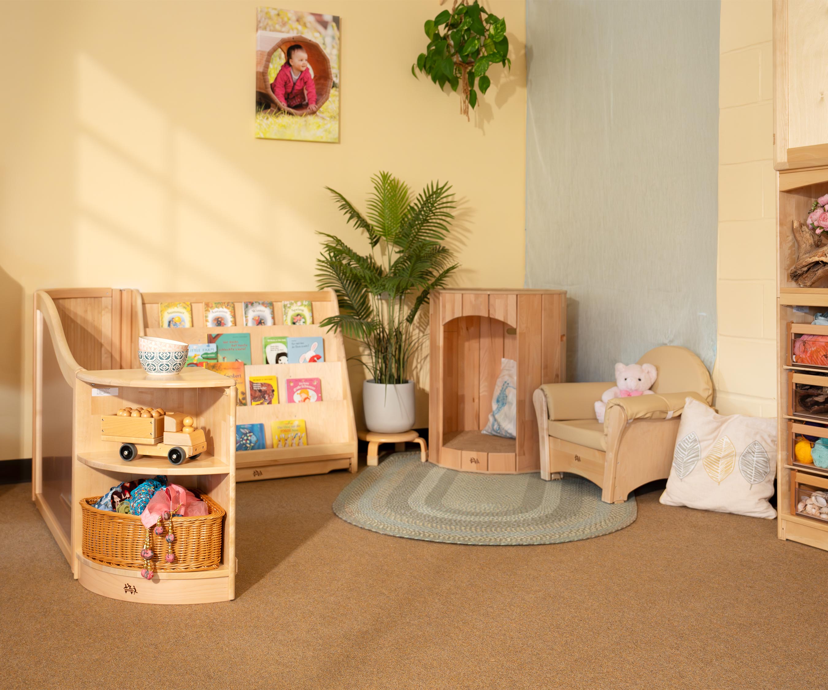 A calm corner set up with natural wooden furniture, a Hollow Nook, a book shelf, and beautifully coloured materials.