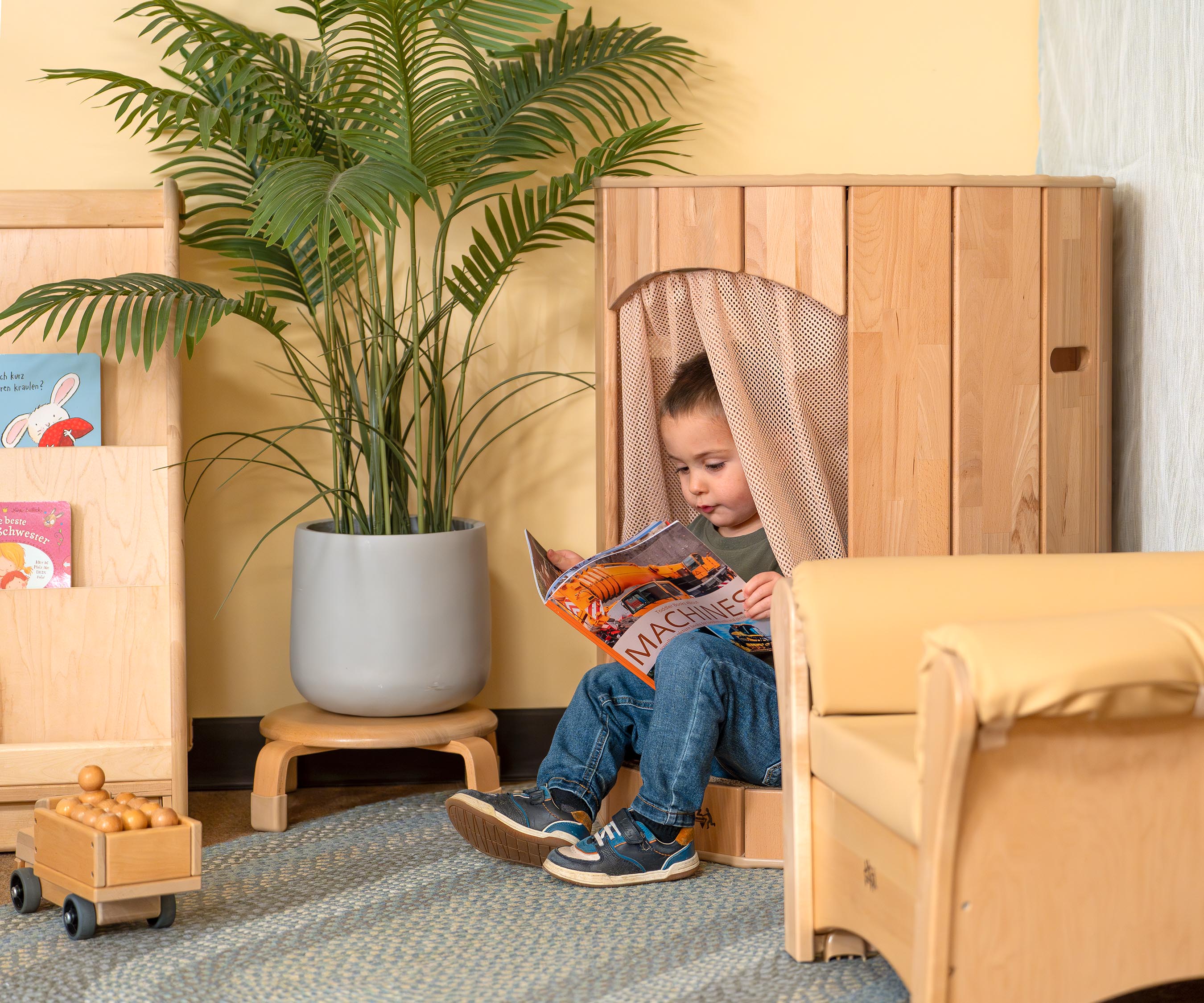 A boy reading a book and sitting in a Hollow Nook with the curtain draped over his shoulder