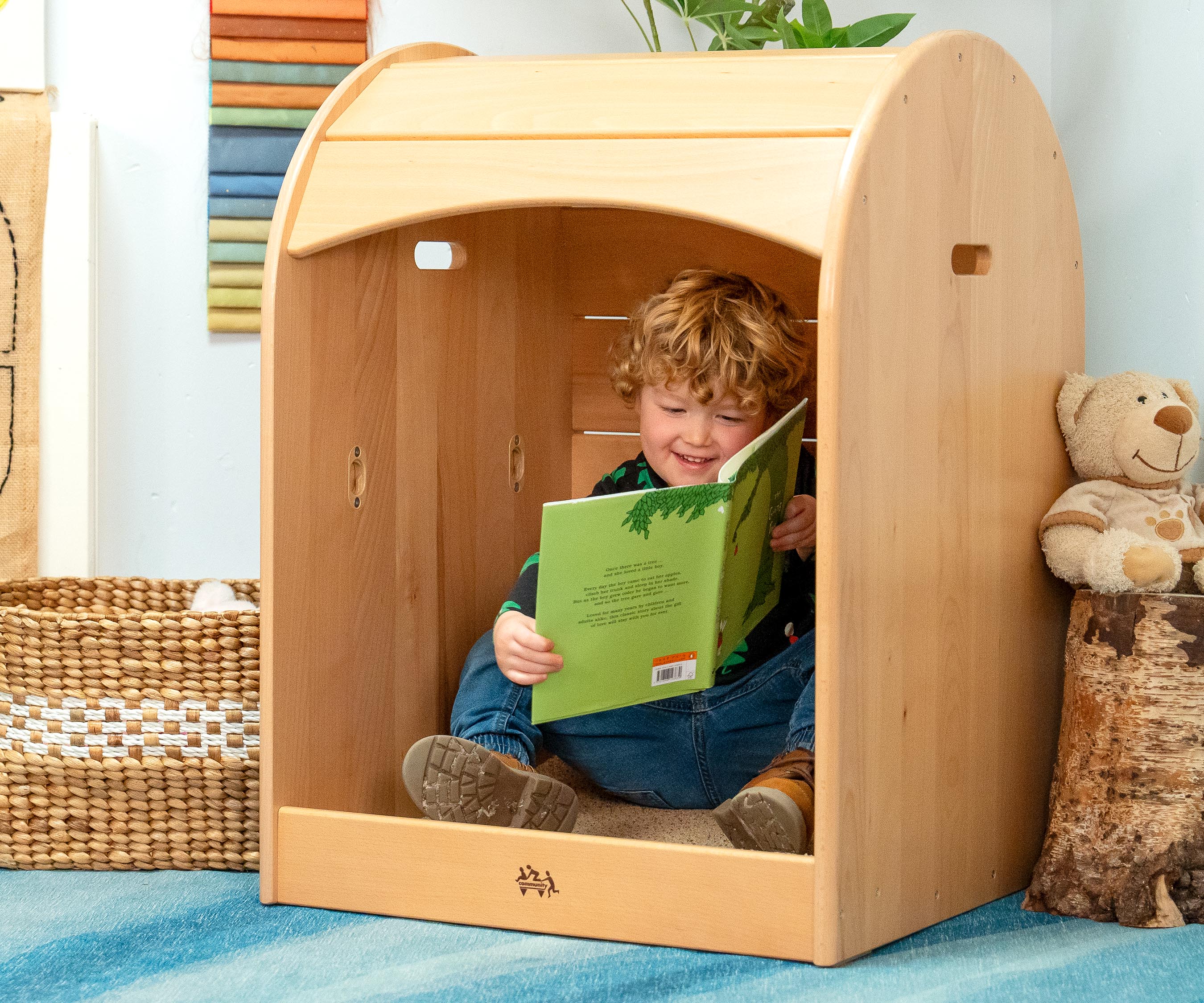 A happy boy wearing jeans and a Christmas tree shirt sitting in a Nest Nook and looking at a book
