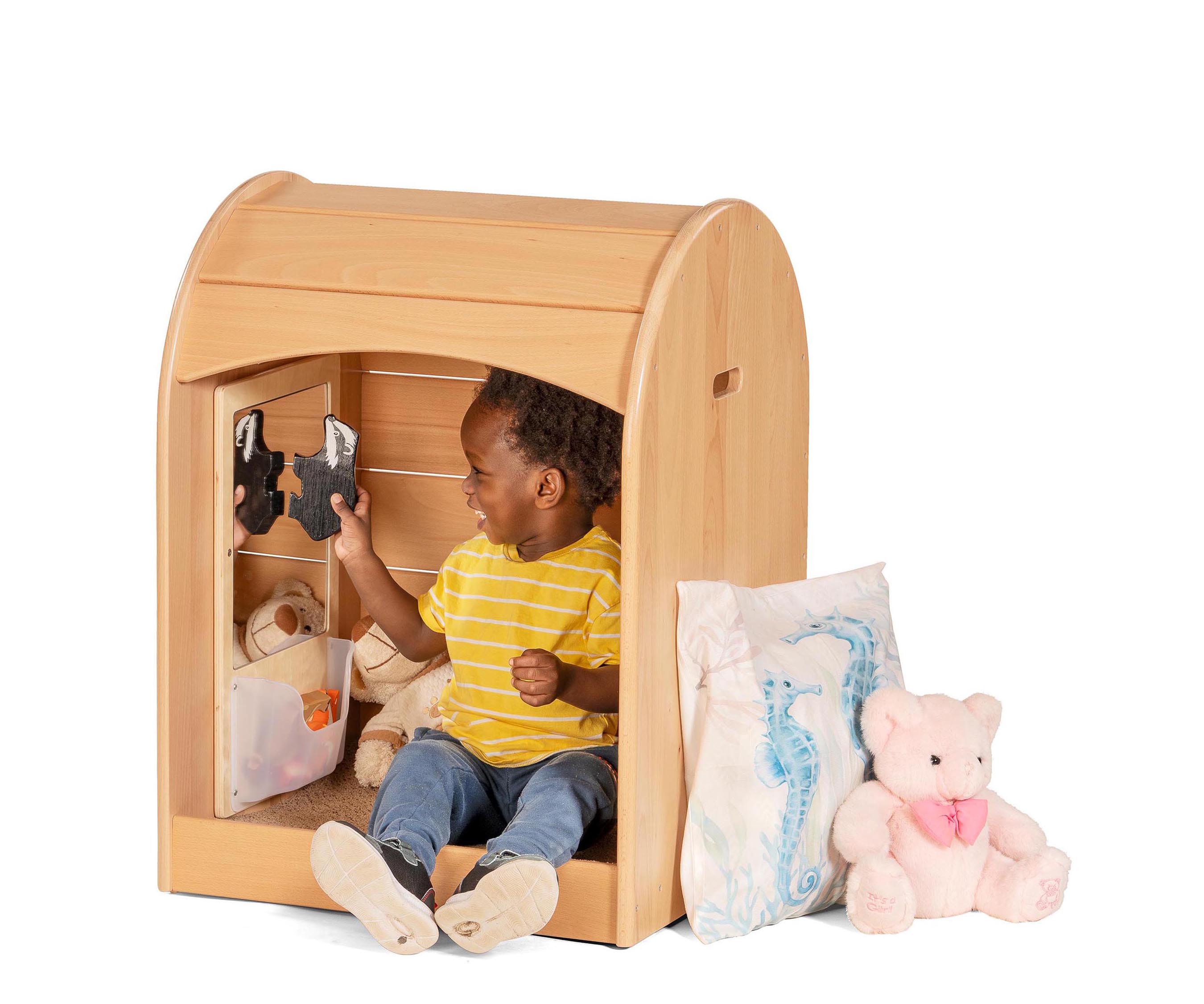 A toddler boy wearing a striped yellow shirt sitting in a Nest Nook at laughing at the wooden painted badger he is holding up to the mirror panel