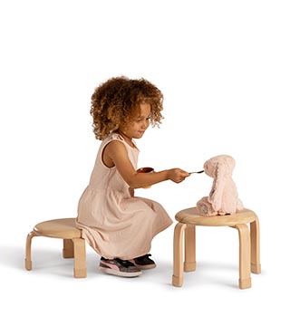 A child sitting on a stacking stool uses a second stool as a table
