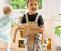 A boy dressed in black shirt and overalls is carrying a stackable wooden stool