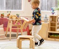 A child carrying a stacking stool with a stack of stools standing on the floor