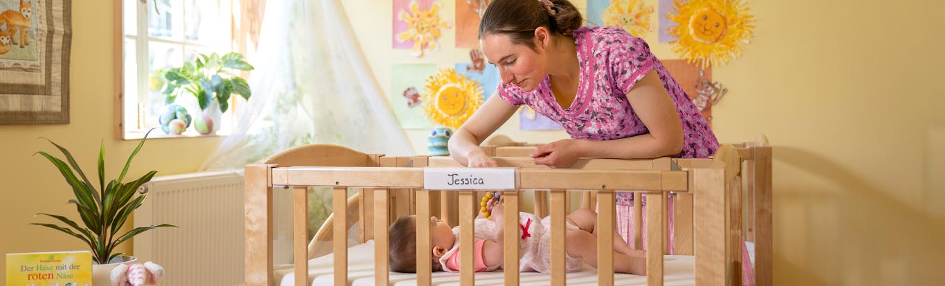 A child in a cot with a mother looking over her.