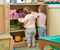 Two babies reaching for toys on solid wood shelf