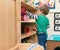 Baby wearing green shirt choosing toy from solid wood nursery shelf