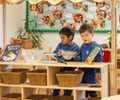 Two reception aged boys exploring with learning materials at a solid wood shelf