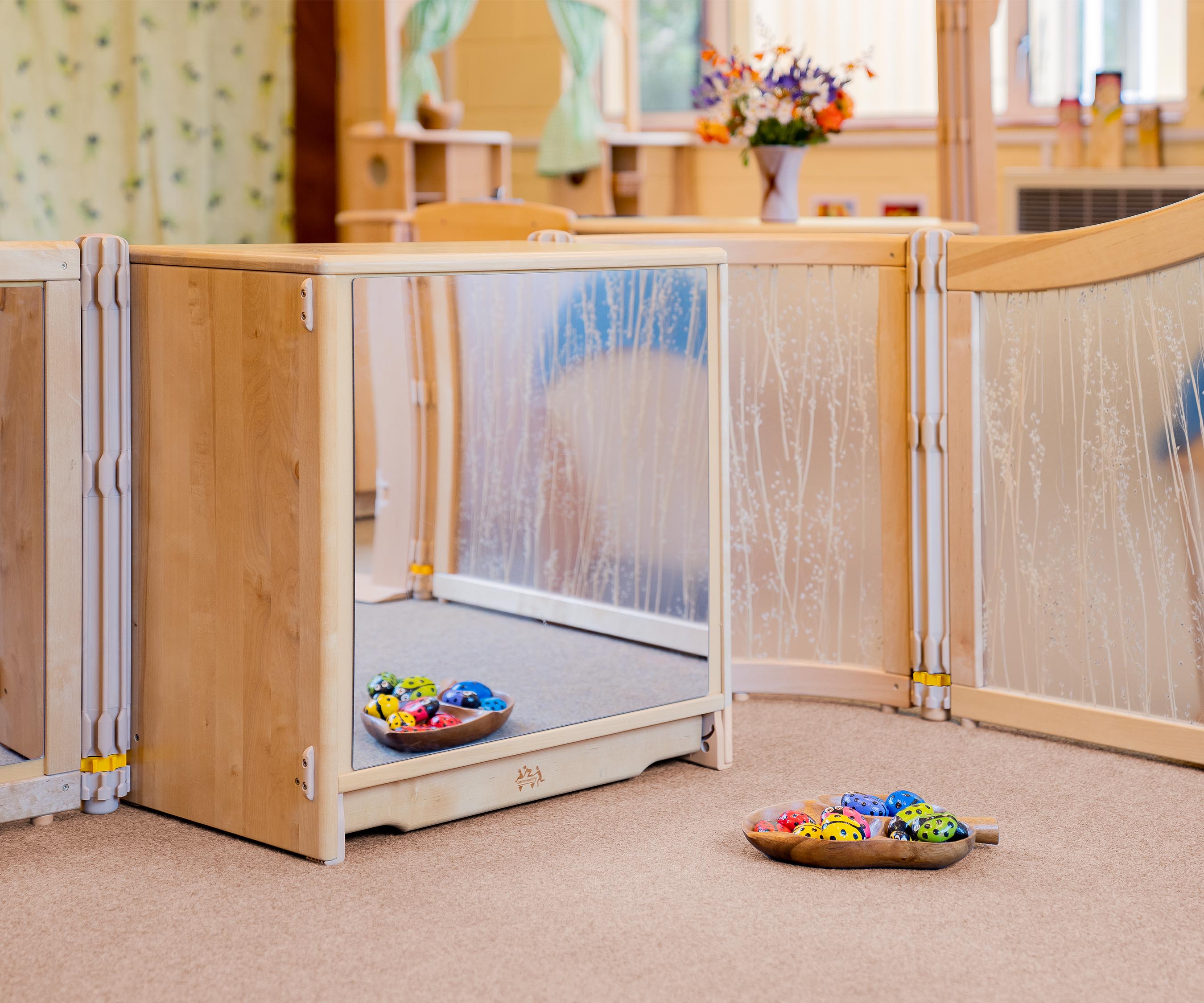 A solid wood school and nursery storage shelf with a mirror cover on the back and a tray of painted rock ladybugs placed in front.