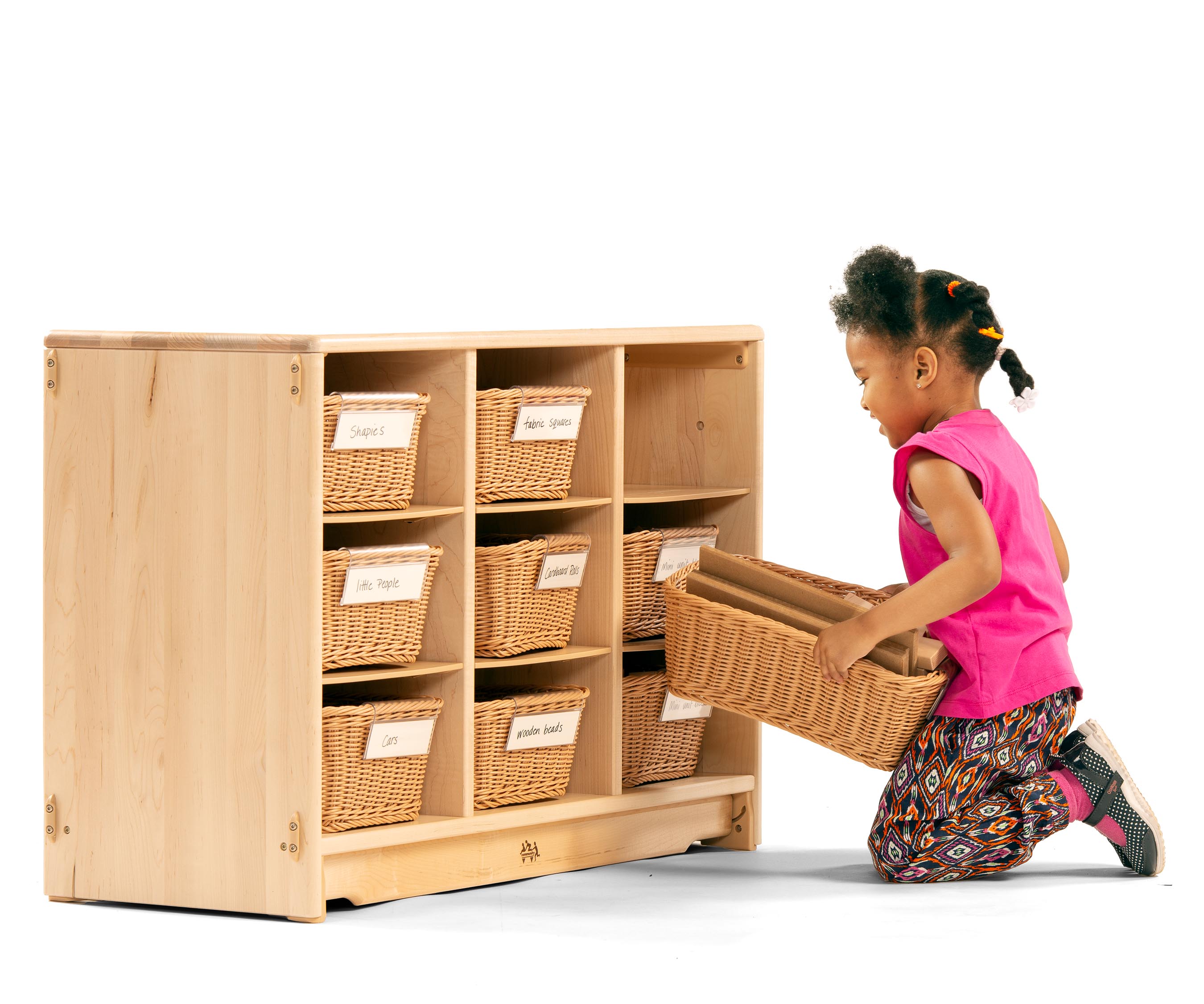 a Preschool girl wearing a pink tank top and flowered leggings pulling a basket of mini unit blocks from a school and nursery storage shelf.