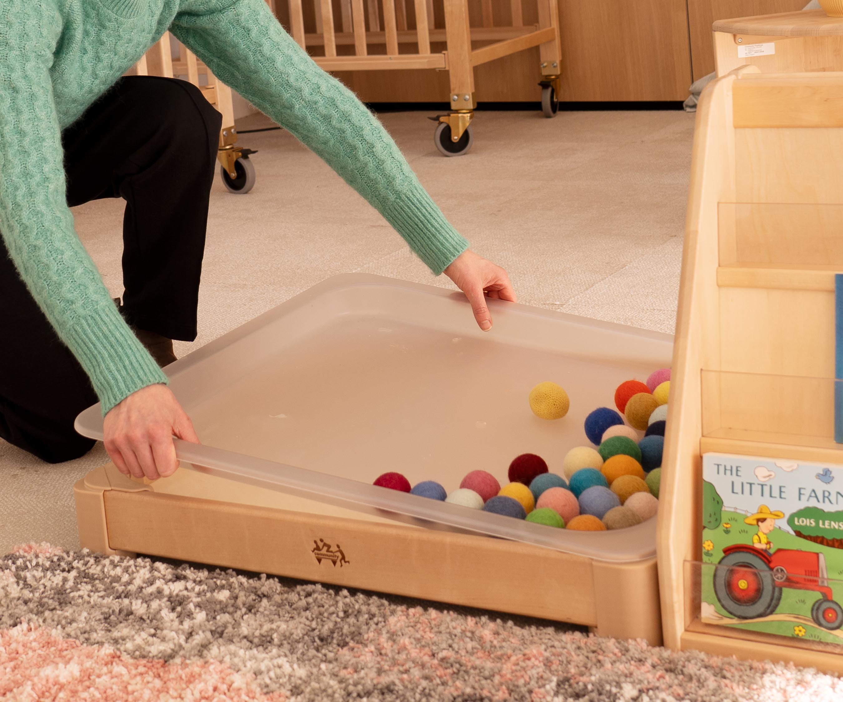 Closeups of a teacher's hand lifting the tray out of an Activity floor tray, which, in contrast to the original tuff tray, is small enough to be transported upright through a standard door frame.