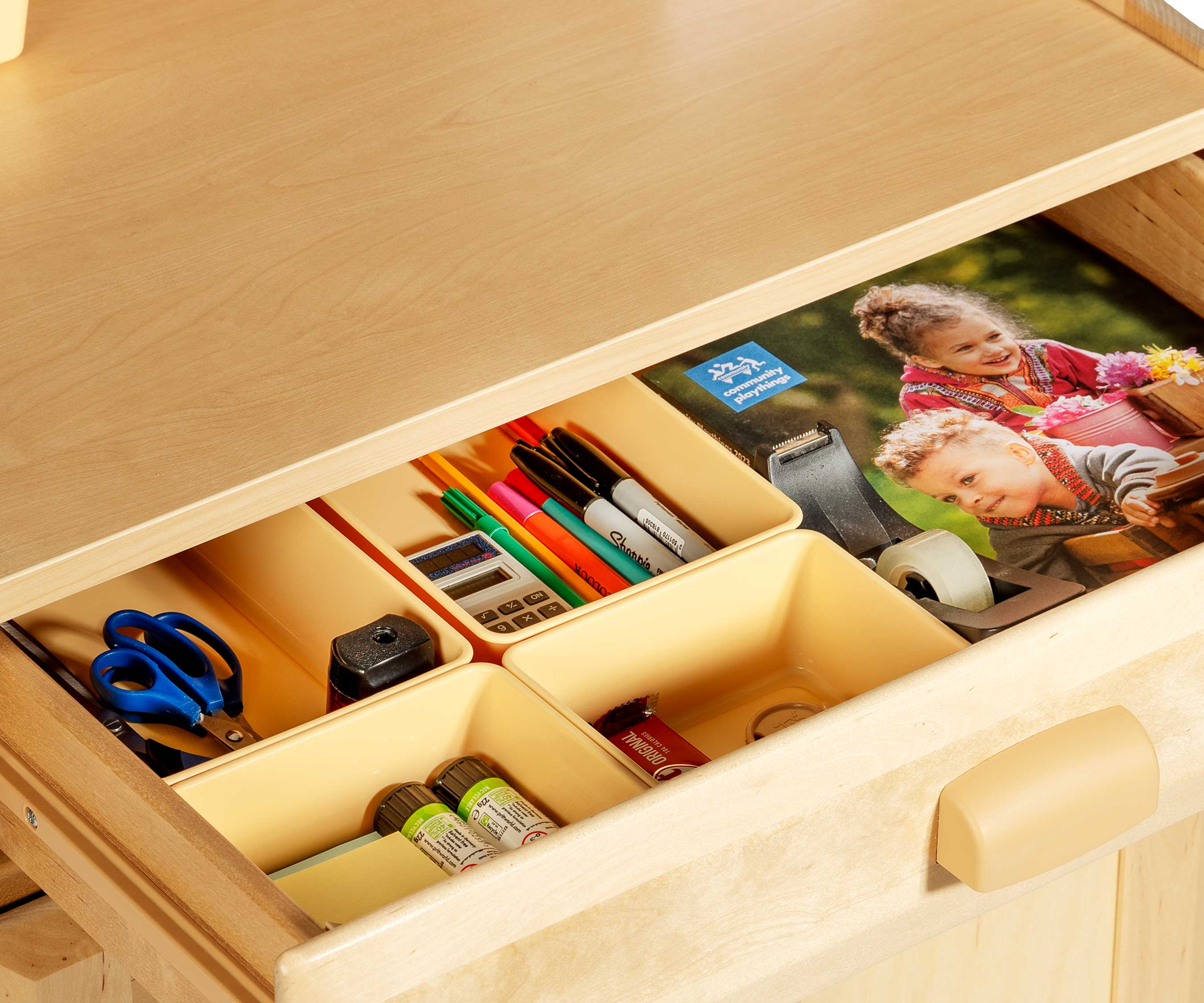 The open drawer of a teacher standing desk, showing office material and an A4 booklet inside