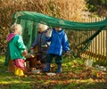three toddlers playing with loose parts under an Outlast arbour