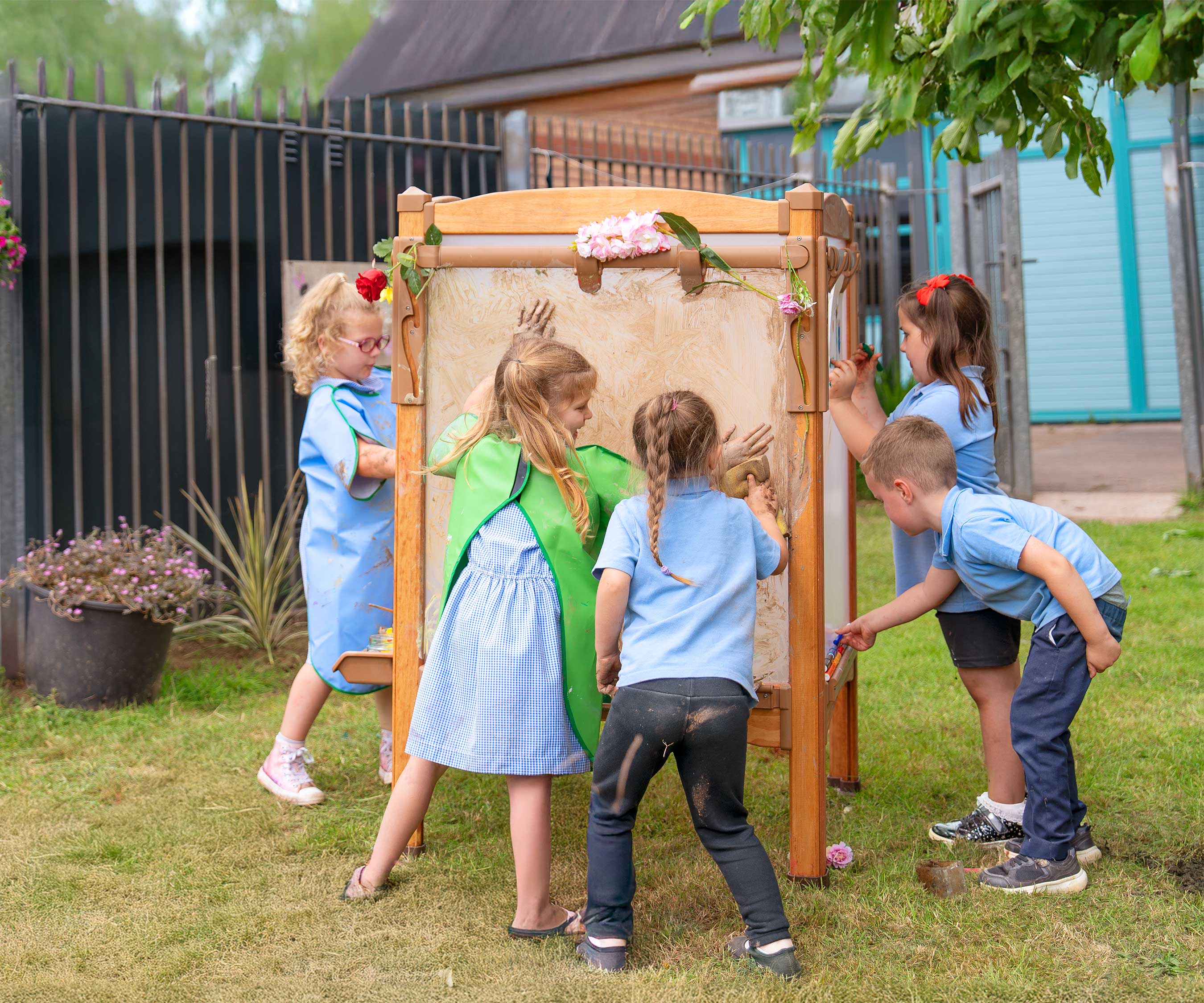A group of five children engaged in messy process art at an outdoor easel.