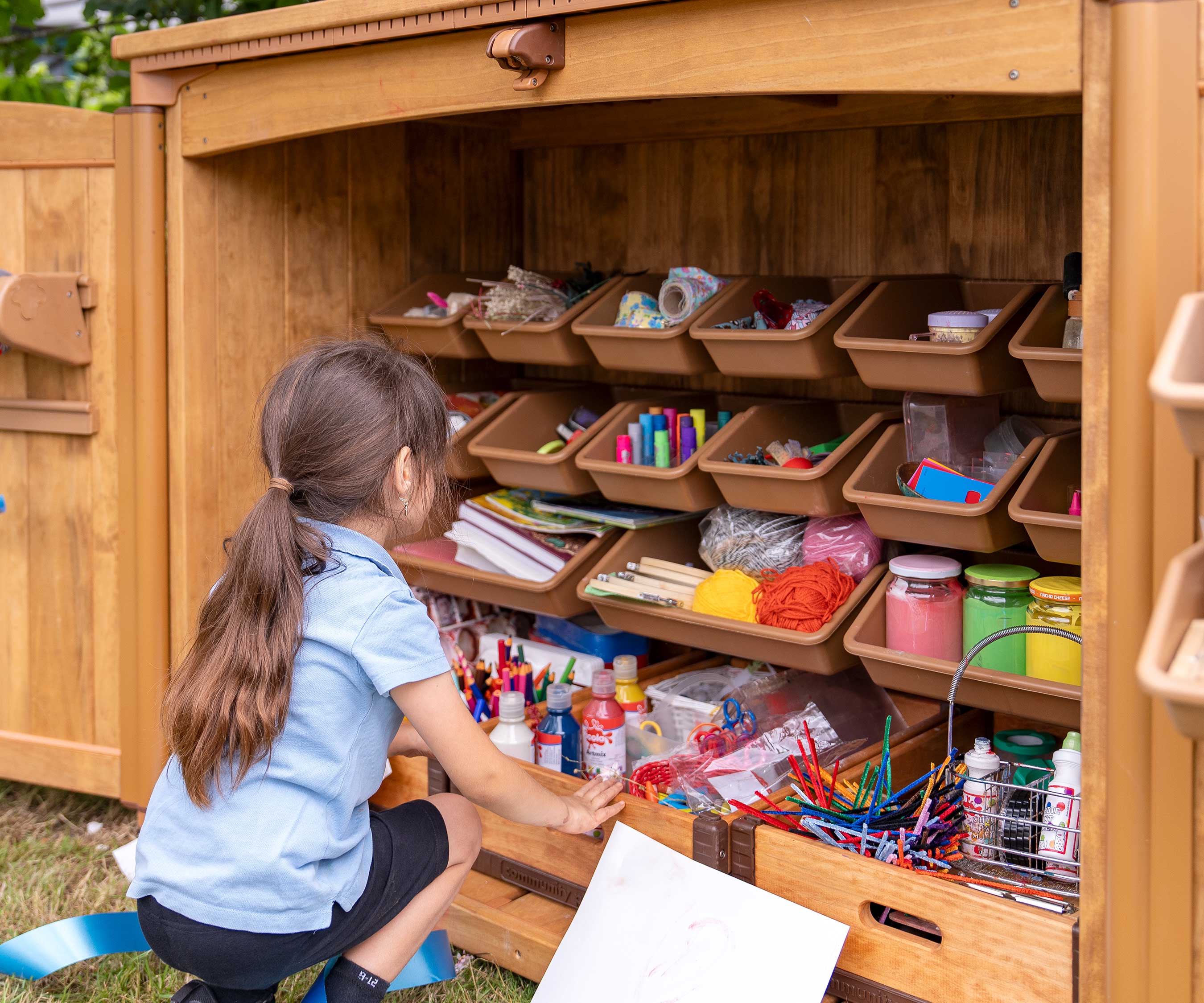 A reception aged girl in an outdoor area looking all the materials stored in an art supply shed.