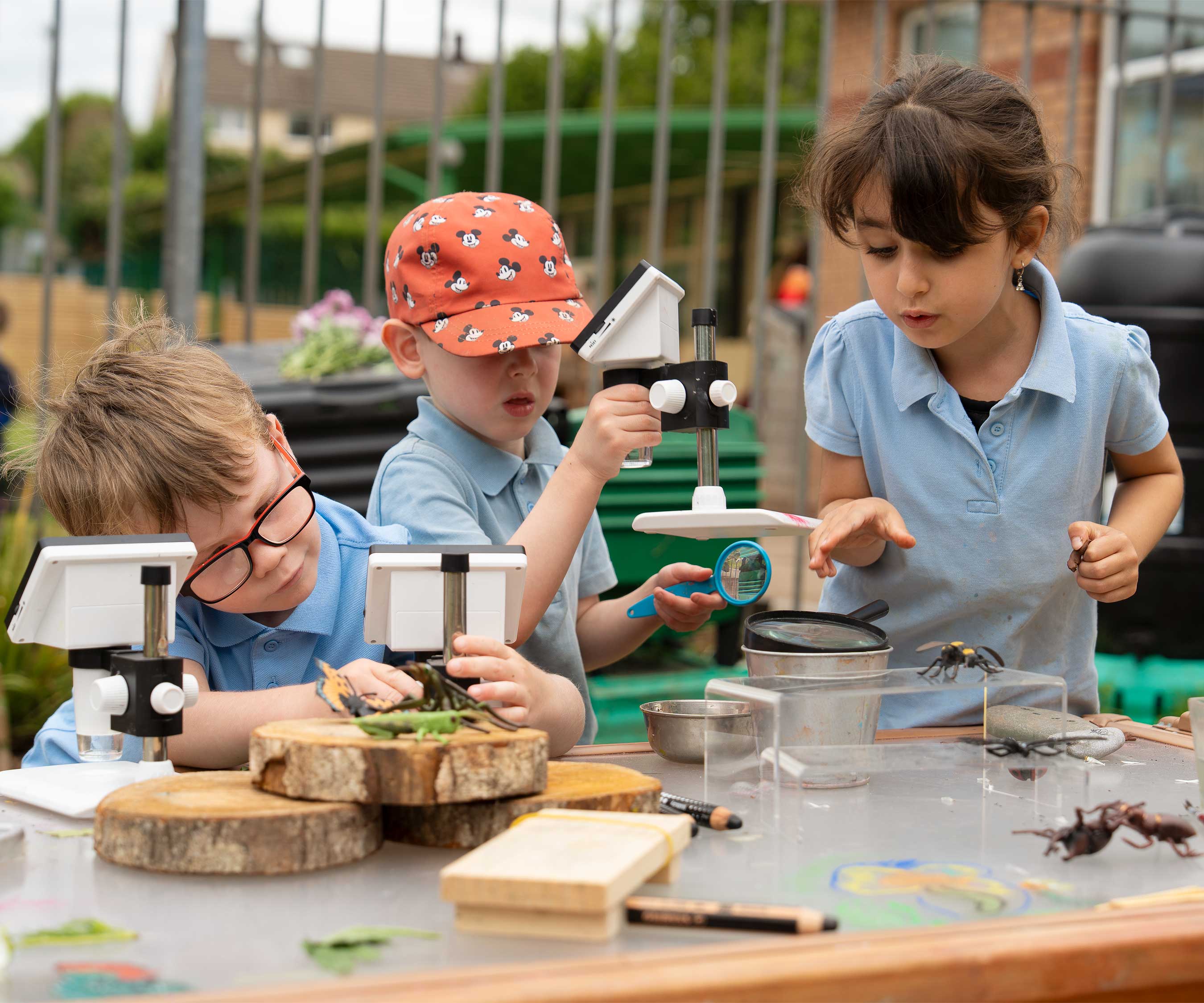 Children at primary school using microscopes and science equipment at an outdoor art table.