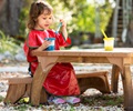 Girl wearing red apron and sitting outside on a bench painting at an outdoor table