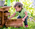 A small child pushes a Nature tray into a toddler mud kitchen