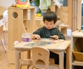 A reception aged boy doing a puzzle at a solid wood table with a play kitchen in the background
