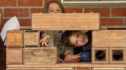 A boy and girl peek through an Outlast block construction