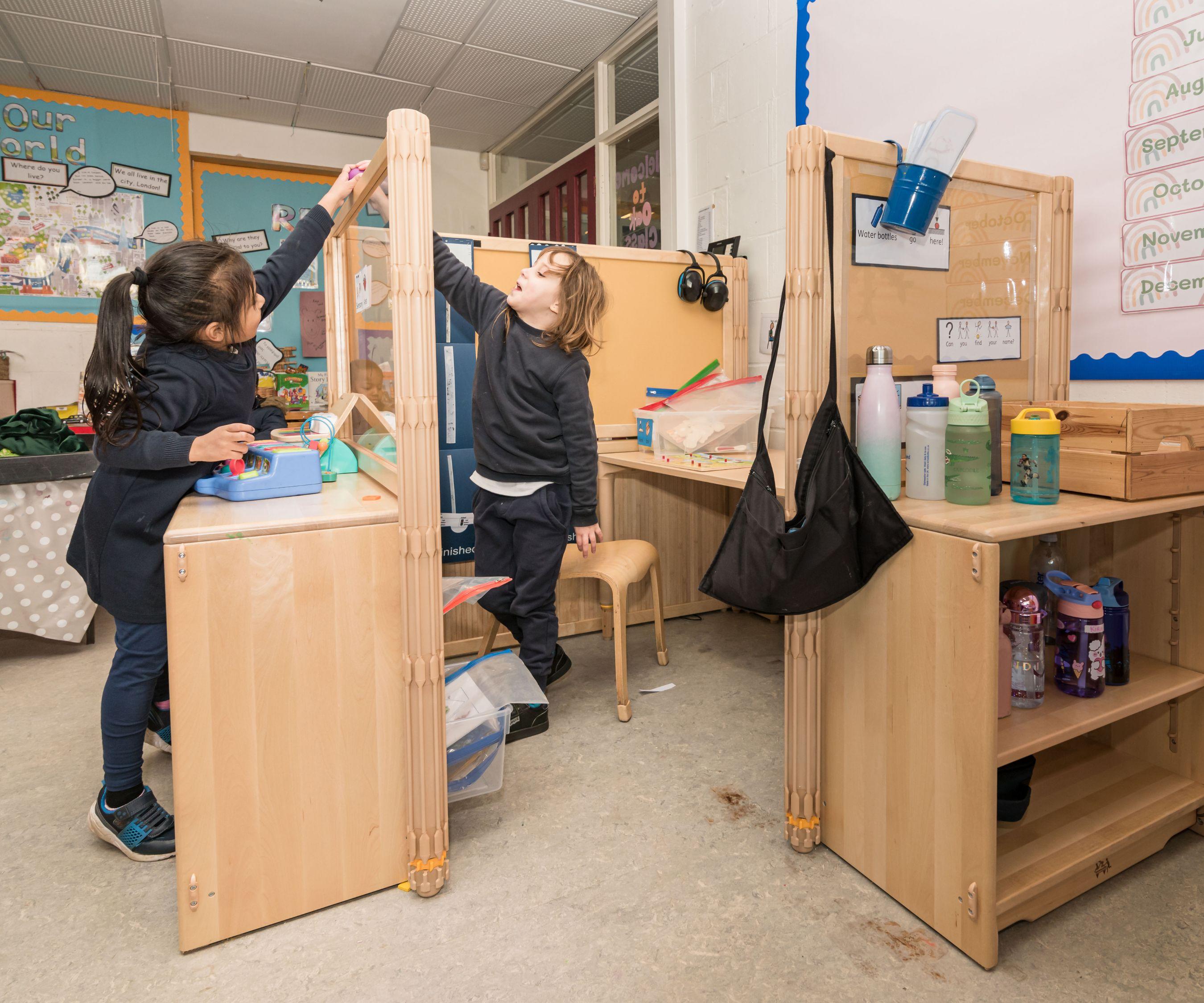 Two young girls playing with toys and reaching up on a wooden primary workstation in a classroom.