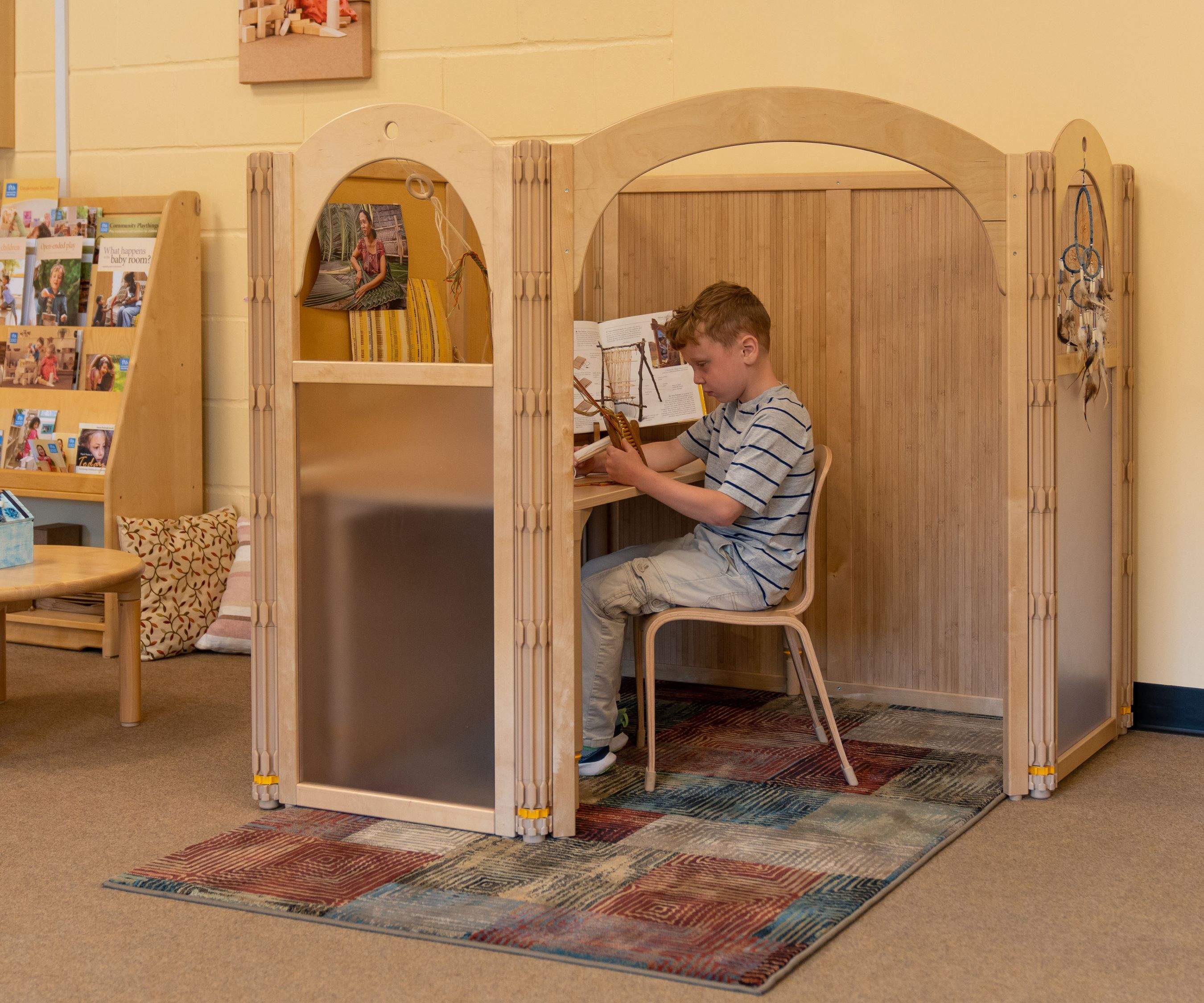 Boy weaving at a compact primary school workstation with a book open on the desk.